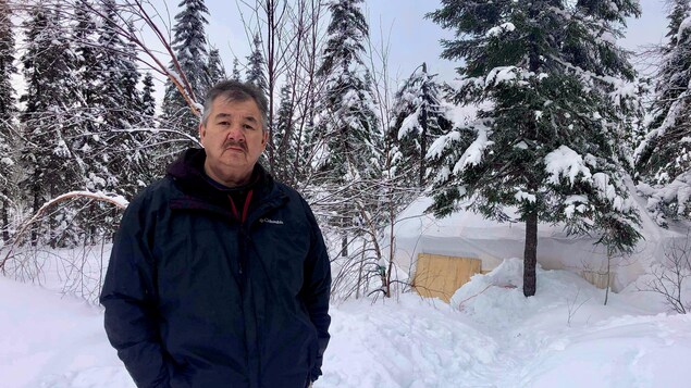 Un homme pose devant une forêt en hiver.