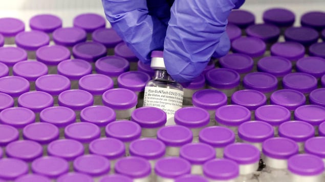 Une main prend une dose du vaccin de Pfizer dans un plateau rempli dans petits flacons de vaccins.