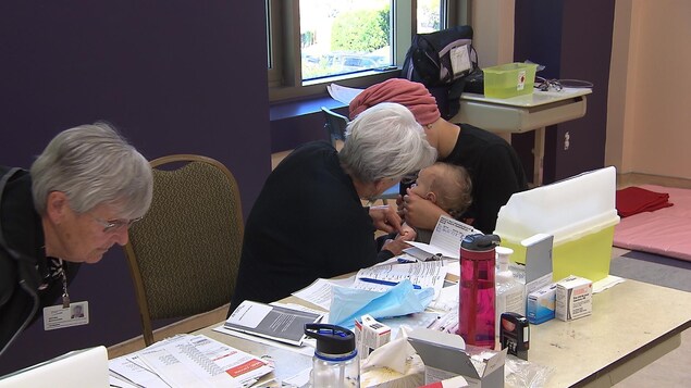 Une femme vaccine un enfant tenu par sa mère.