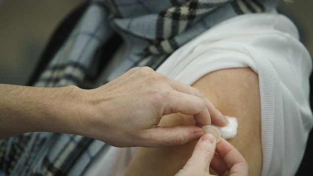 Un travailleur de la santé applique de la ouate et un pansement sur le bras d'une patiente âgée venant tout juste de recevoir son vaccin.