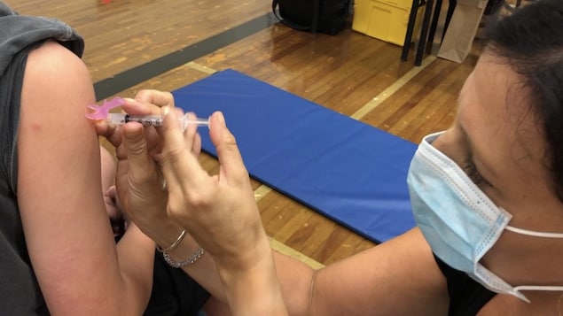 Une infirmière portant un masque vaccine une adolescente.