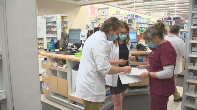 Un pharmacien discute avec un infirmière derrière le comptoir d'ne pharmacie.
