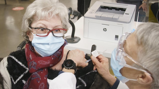 Une femme masquée lève les sourcils en se faisant vacciner.