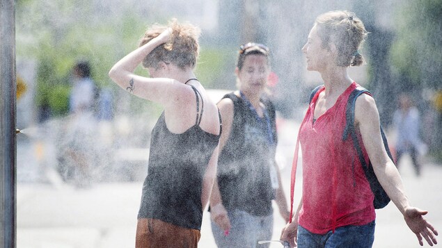Trois femmes profitent d'un jet d'eau pour se rafraîchir.