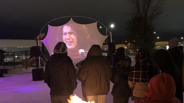 Une dizaine de personnes regarde la projection à l'extérieur. Certains sont près du feu pour se réchauffer.