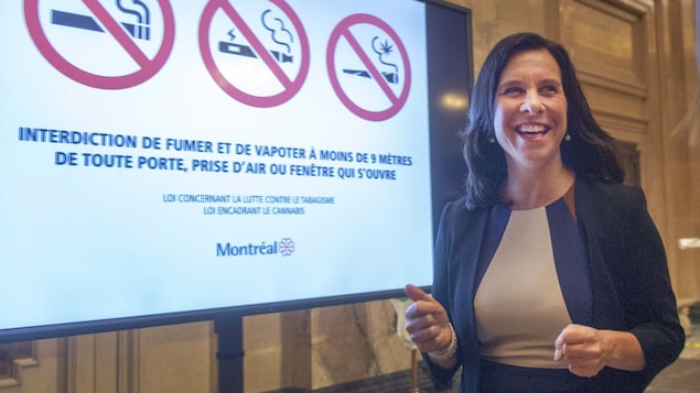 La mairesse Valérie Plante à côté d'un panneau indiquant l'interdiction de fumer ou de vapoter à moins de 9 mètres d'une porte, prise d'air ou fenêtre qui s'ouvre.