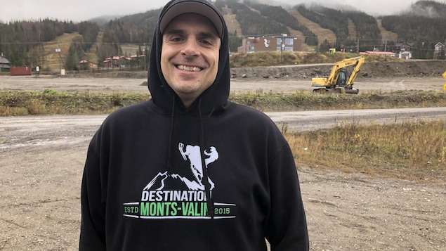Un homme avec un chandail à capuchon pose devant un stationnement.