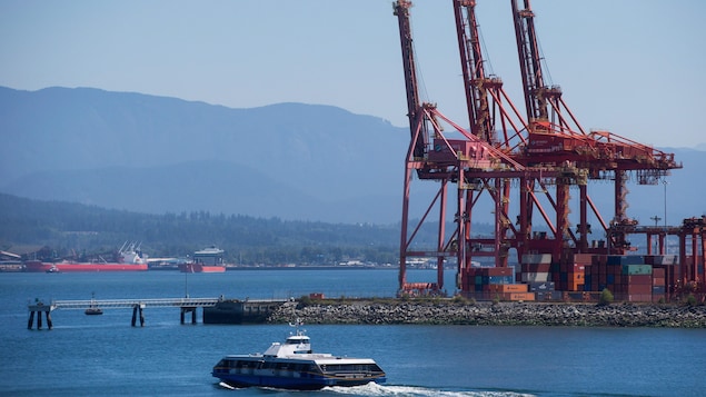 Un Seabus (bateau de transport de passagers) passe devant les installations du port de Vancouver avec des navires en arrière-plan.