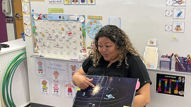 L'enseignante en classe d'accueil Vanessa Ibanez. Elle montre aux enfants un livre sur le système solaire. 