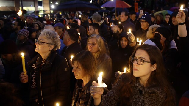 Des dizaines de personnes rassemblées tiennent une chandelle à la main.