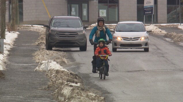 Une cycliste et son garçon partagent la route avec une voiture qui les suit de près