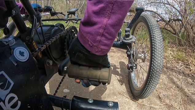 Une athlète paralympique utilise avec l'aide de ses mains un vélo spécialement conçu pour se déplacer en nature.