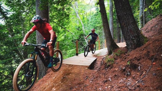 Deux sportifs sur des vélos de montagne qui se suivent sur un chemin forestier.