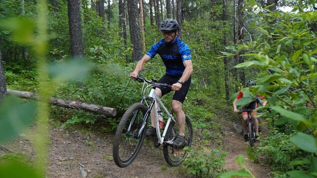 Un homme en vélo dans un sentier de vélo de montagne suivi par deux autres cyclistes.