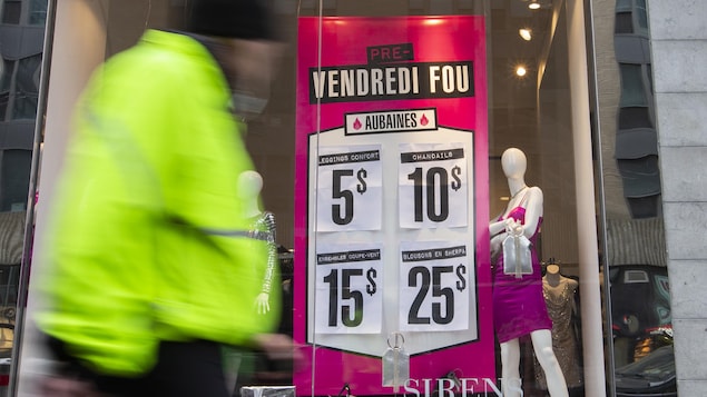 Un passant devant une vitrine de magasin où sont affichées des soldes.