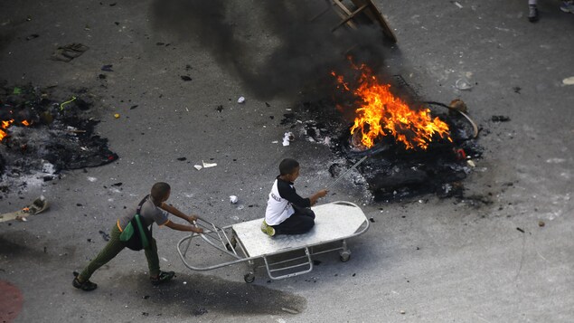 Deux enfants jouent dans une rue de Caracas, entre des monticules de déchets enflammés