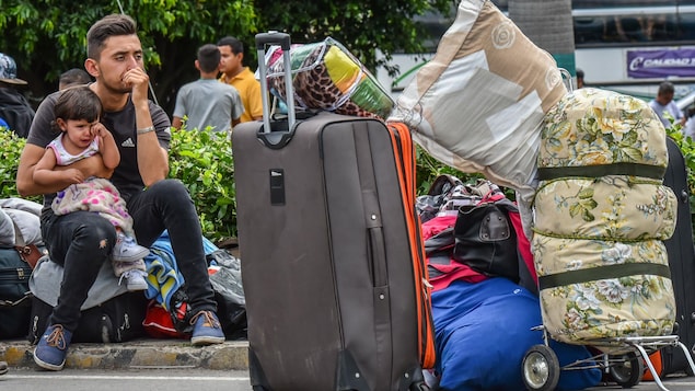 Un jeune homme pensif assis sur une valise tient une fillette qui pleure dans ses bras. Un jeune homme pensif assis sur une valise tient une fillette qui pleure dans ses bras.