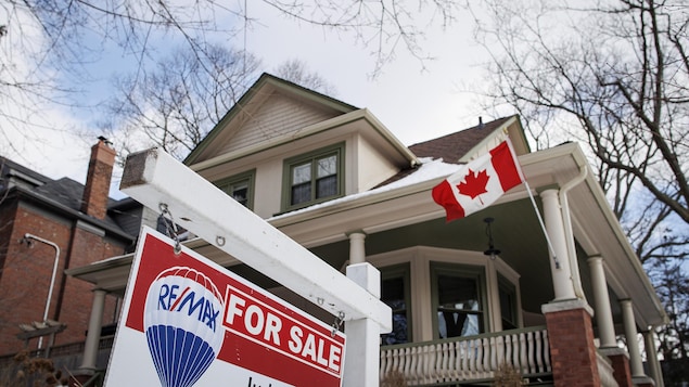 لافتة أمام منزل تفيد بأنه معروض للبيع، ويبدو العلم الكندي مرفوعاً على أحد أعمدته.