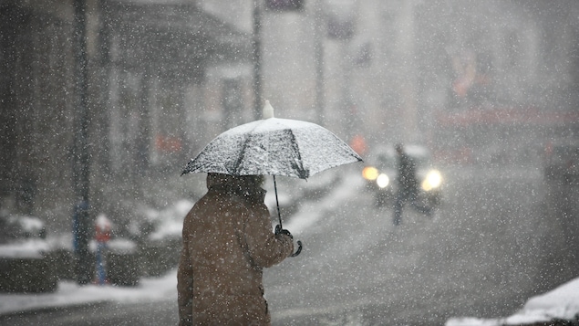 Un homme marche avec un parapluie dans une rue enneigée.