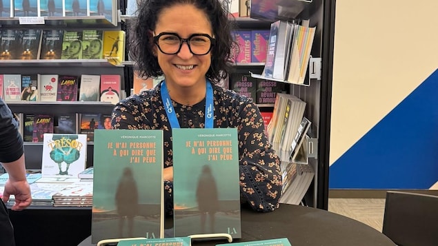 Une femme brune pose à côté de livres. 
