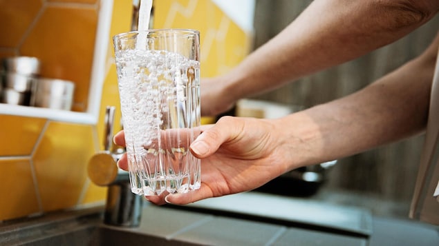 Des mains remplissent un verre d'eau à un robinet d'évier.