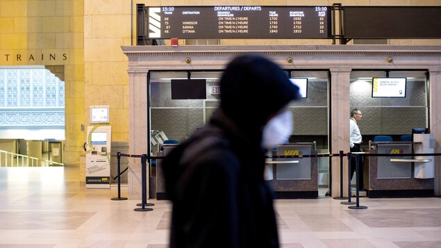 Un homme masqué passe devant un comptoir de VIA Rail à la gare Union de Toronto.