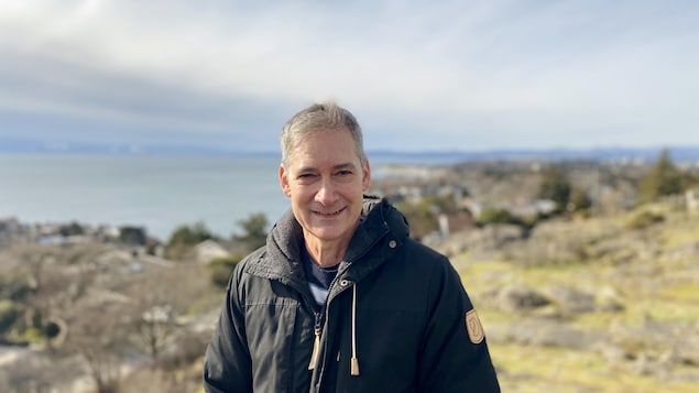 Un homme sourit à la caméra, derrière lui un paysage 