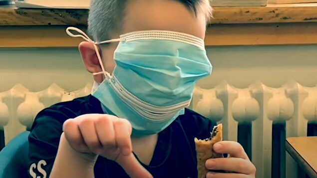 Un enfant porte deux masques superposés dans son visage, lui dissimulant les yeux. Il tient une barre tendre dans sa main gauche.