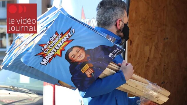 Un homme masqué transporte des pancartes syndicales.