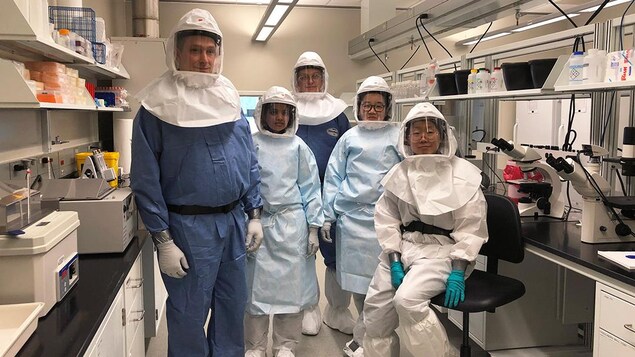 Des travailleurs dans un laboratoire posent pour le photographe avec des habits pour se protéger.