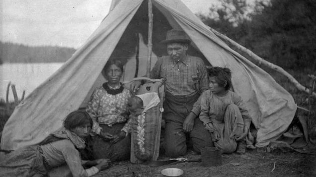 Une vieille photo montrant un père et une mère autochtone dans une tente avec deux enfants.
