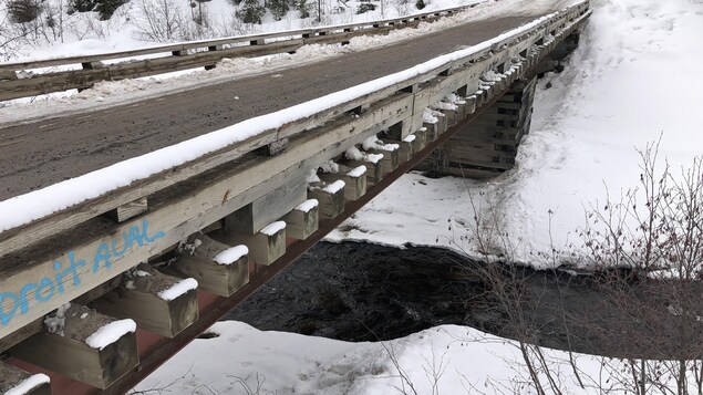 Un pont en bois qui semble vieux et usé et qui passe par-dessus une rivière. 