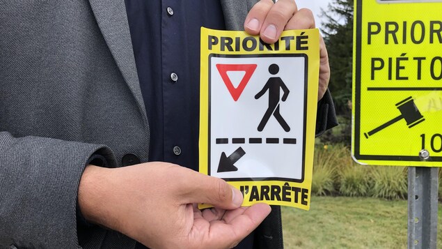 Une personne se trouvant à proximité d'une traverse pour les piétons tient une vignette de sensibilisation.