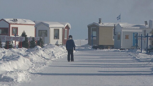 Un marcheur arpente le sentier principal du village sur glace, entouré de maisonnettes.
