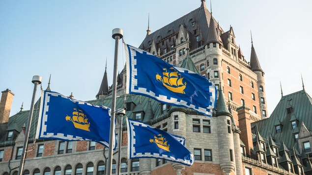 Trois drapeaux du logo de la Ville de Québec en avant du Château Frontenac.