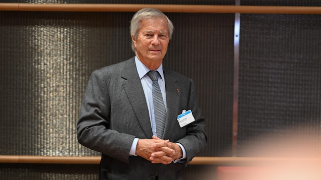 Un homme habillé de gris a les mains jointes. 