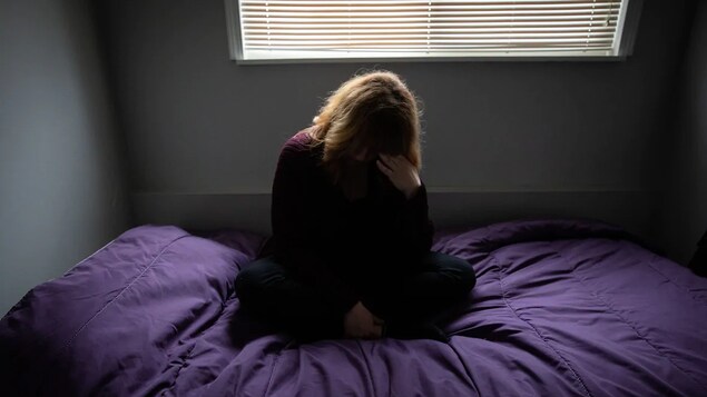 Une femme est assise sur son lit et se tient la tête.