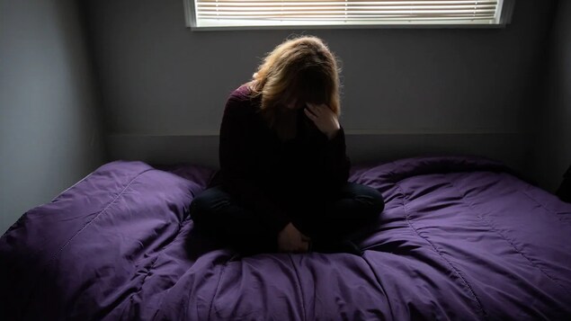 Une femme est assise sur son lit et se tient la tête.