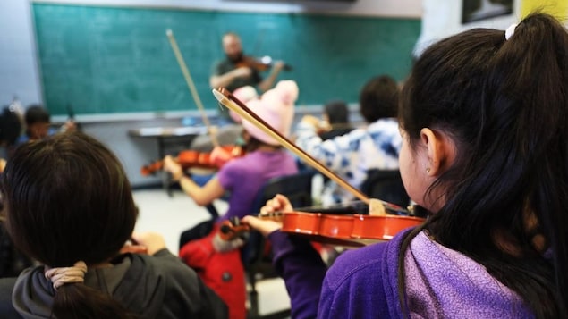 Des jeunes qui jouent du violon dans une classe
