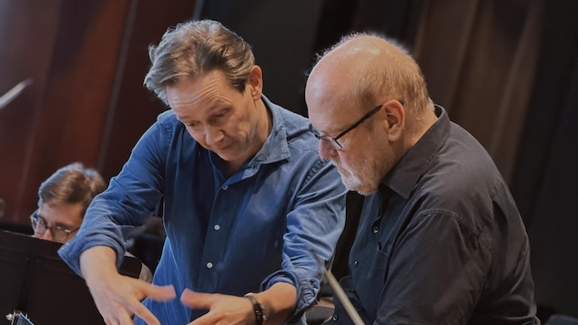 Deux hommes se consultent lors d'une séance de répétition d'un orchestre à cordes. 
