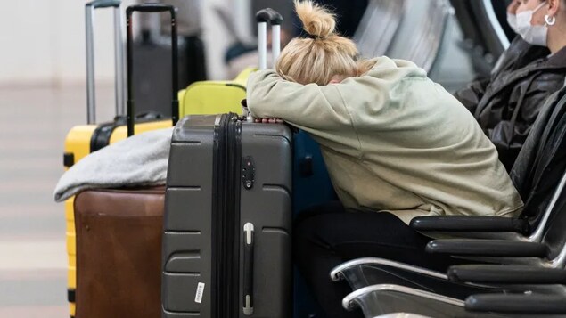 A woman rests her head on her luggage as she awaits the results of her COVID-19 test at Ronald Reagan Washington National Airport, Dec. 29, 2021. The U.S. CDC has added Canada to the list of countries it's advising Americans to avoid due to COVID-19 cases. 