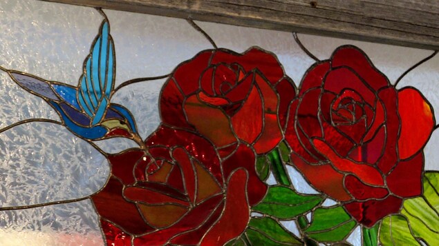 Un vitrail représentant un colibri butinant un rose rouge.