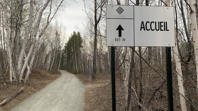 Un sentier en gravier dans une forêt, avec une affiche annonçant l'accueil à 865 mètres en avant-plan.