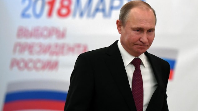Vladimir Poutine est devant une affiche électorale annonçant le vote.
