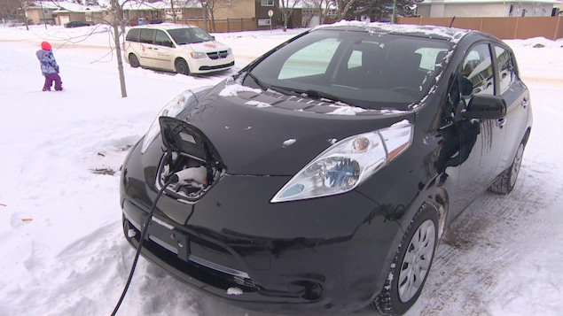 Une voiture est branché à un cable électrique dans un temps enneigé.
