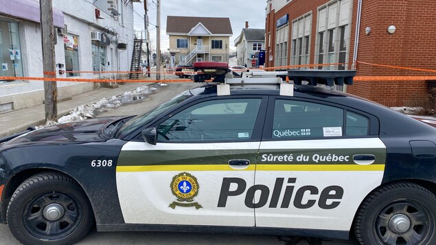 Une voiture de la Sûreté du Québec et un ruban orange dans la rue. 