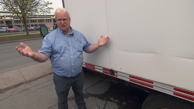 Pierre Gravel se tient debout, à côté d’un camion, avec les bras en l’air.