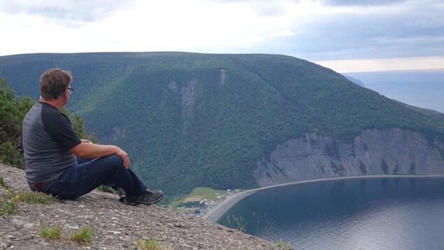 Assis au sommet du mont Saint-Pierre, un homme regarde les sommets et une baie du fleuve Saint-Laurent.