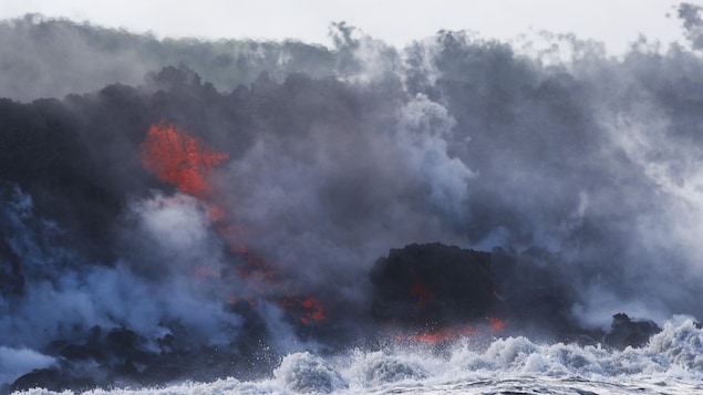 Entourée de fumée, une coulée de lave tombe dans une vague. 