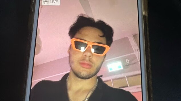 Photo d'un téléphone cellulaire qui affiche l'image d'un homme qui porte des lunettes de soleil aux bords orange.